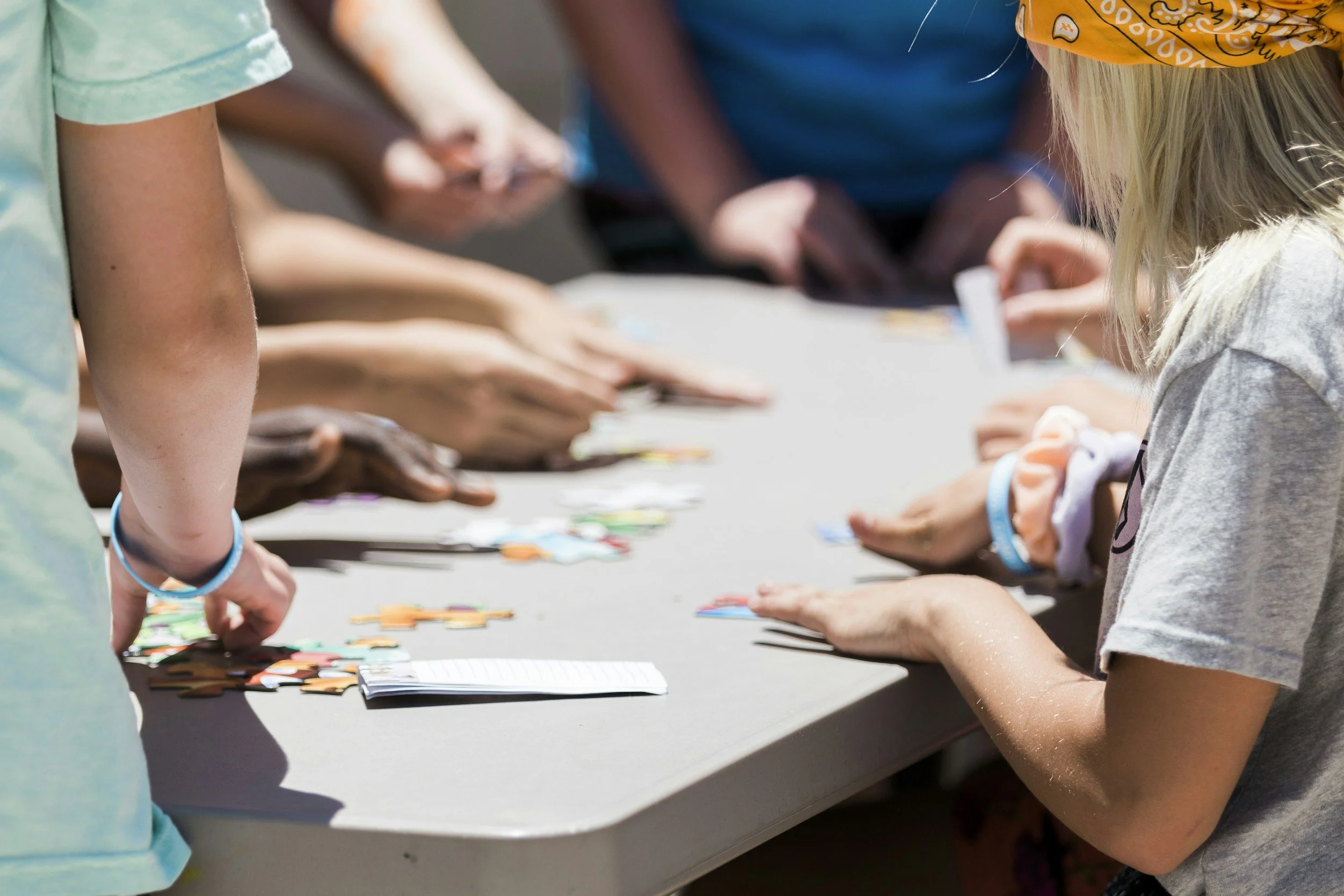 Children working on a puzzle at a table outdoors.